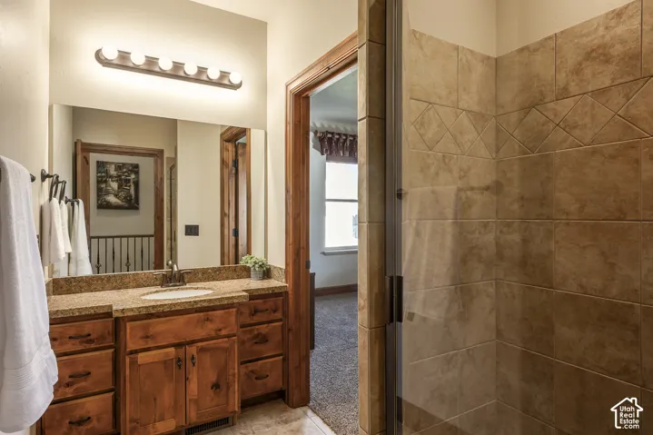 Bathroom featuring a wood vanity with a stone countertop, an integrated sink, a full-width mirror, and a tiled shower enclosure with a glass door