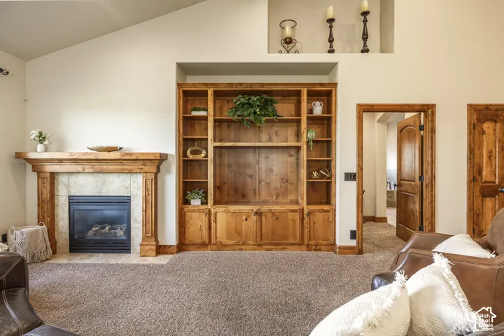Vaulted ceiling room featuring a natural stone fireplace with a thick wood mantel, custom built-in wood shelving with lower cabinetry, and recessed display niche