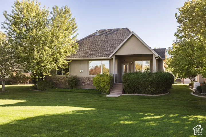Exterior featuring a stucco facade with stone veneer accents, a covered patio with stairs, and a multi-pitched roofline set within a mature landscape