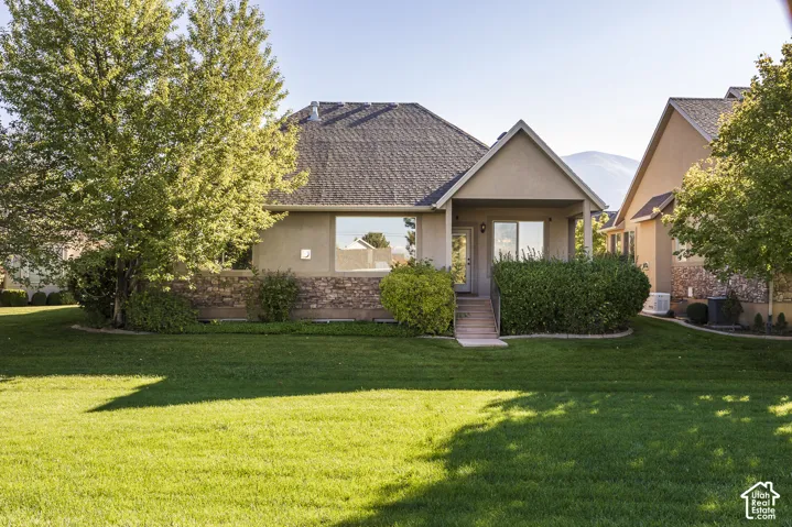 Rear exterior featuring stucco siding, stone masonry accents, a covered porch, and expansive manicured lawn