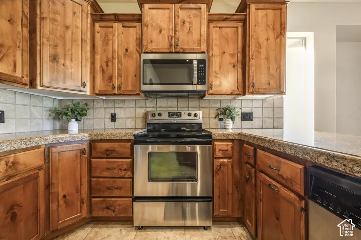 Kitchen featuring stained wood cabinetry, stone-surface countertops, square tile backsplash, and stainless steel appliances
