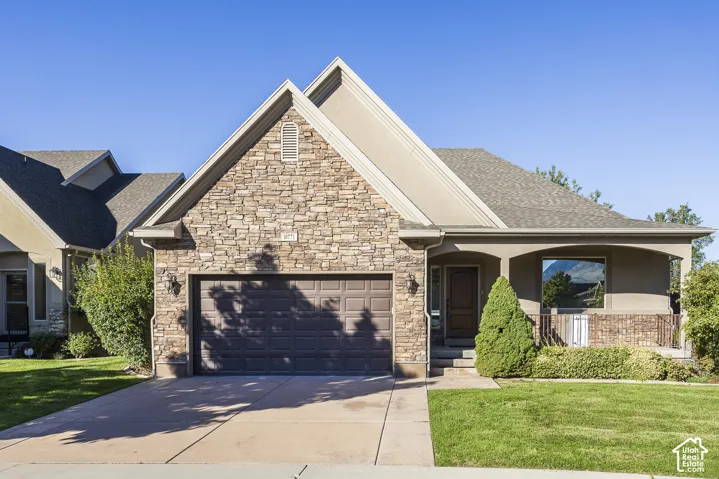 Exterior featuring stone veneer siding, dual-pitched gabled rooflines, a covered front porch, and a concrete driveway leading to an attached two-car garage