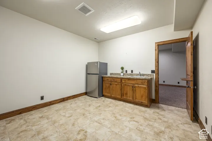 Wet bar area featuring custom wood cabinetry, stone-finish countertops, an integrated sink, and tile flooring
