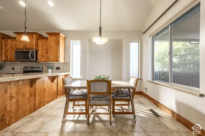 Kitchen featuring stained wood cabinetry, stone-finish countertops, tile flooring, and vaulted ceilings with pendant lighting