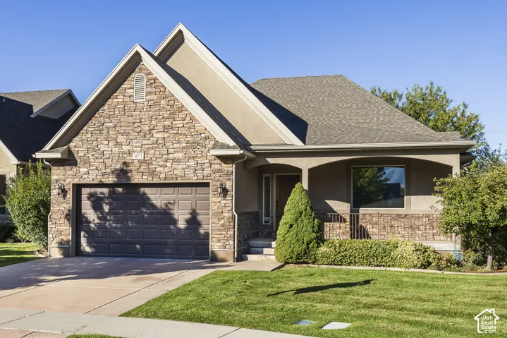 Exterior featuring stone veneer siding, dual gabled rooflines, a covered front porch, and an attached two-car garage