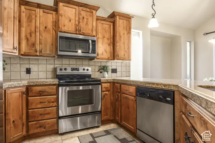 Kitchen featuring knotty wood cabinetry, stone countertops, stainless steel appliances, tiled backsplash, and pendant lighting