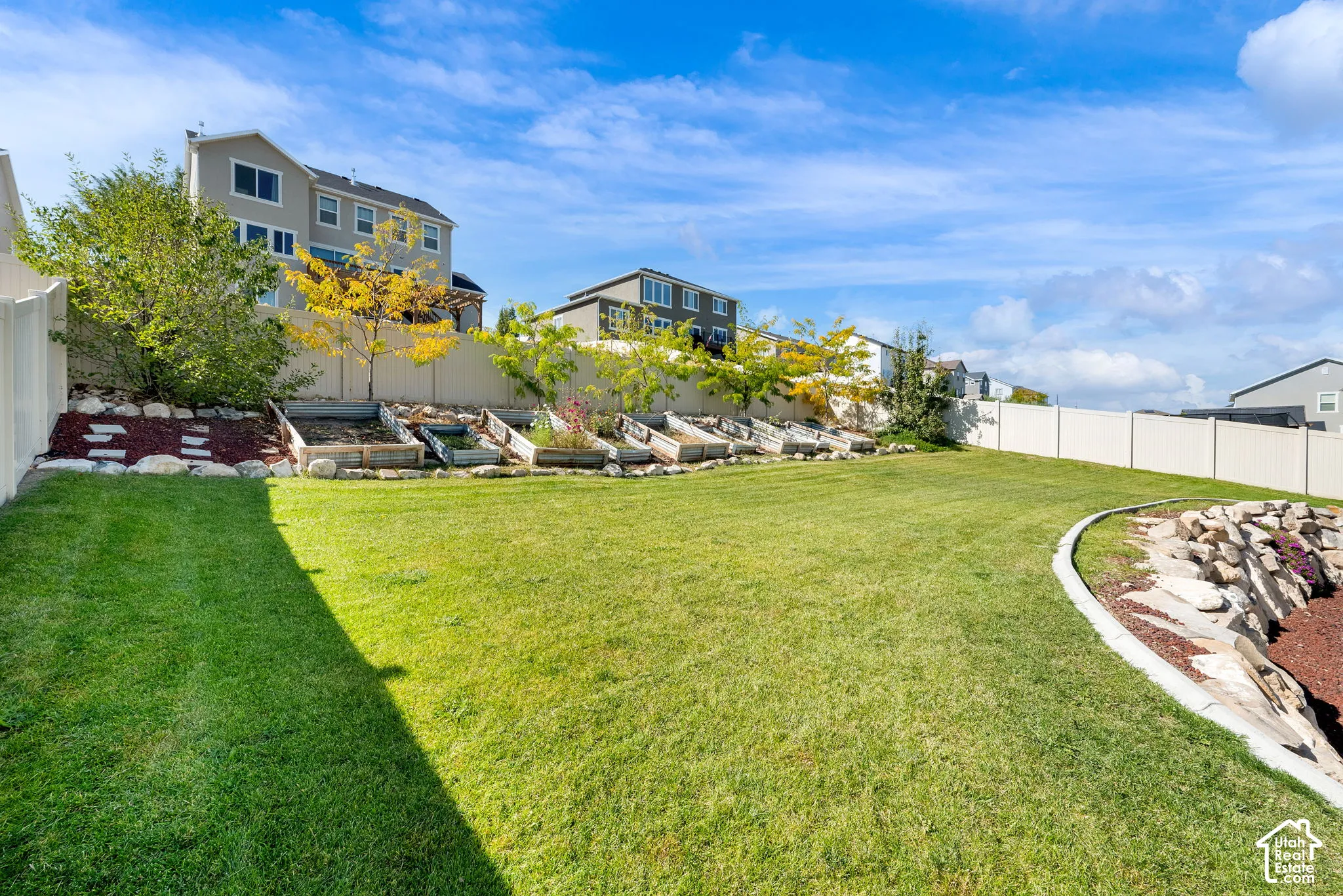 Backyard featuring a manicured lawn, tiered garden beds, stone hardscaping, and perimeter privacy fencing