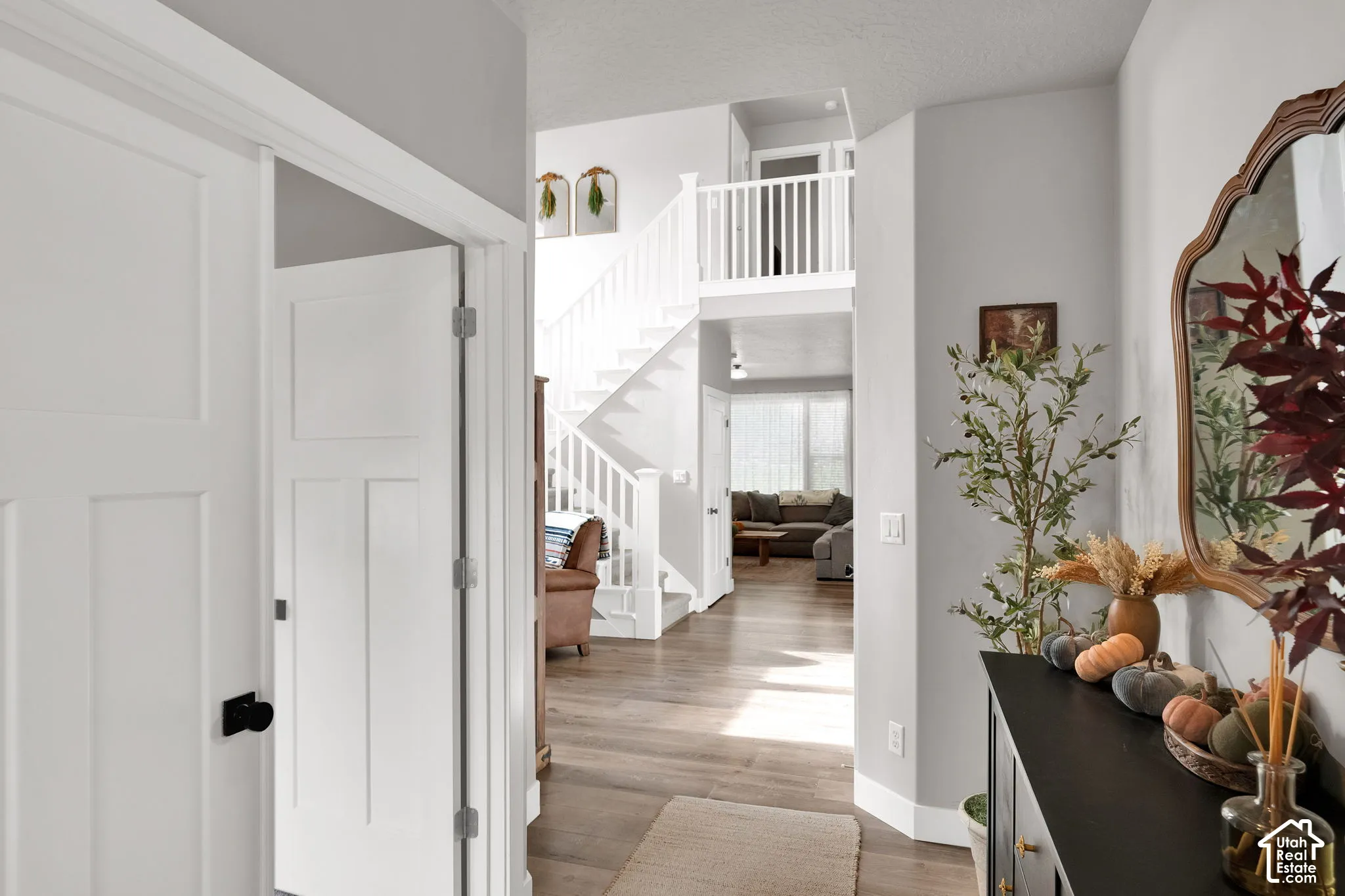 Foyer featuring wood-finish flooring, a white staircase with a wooden handrail and balusters, and multi-panel doors with matte black hardware