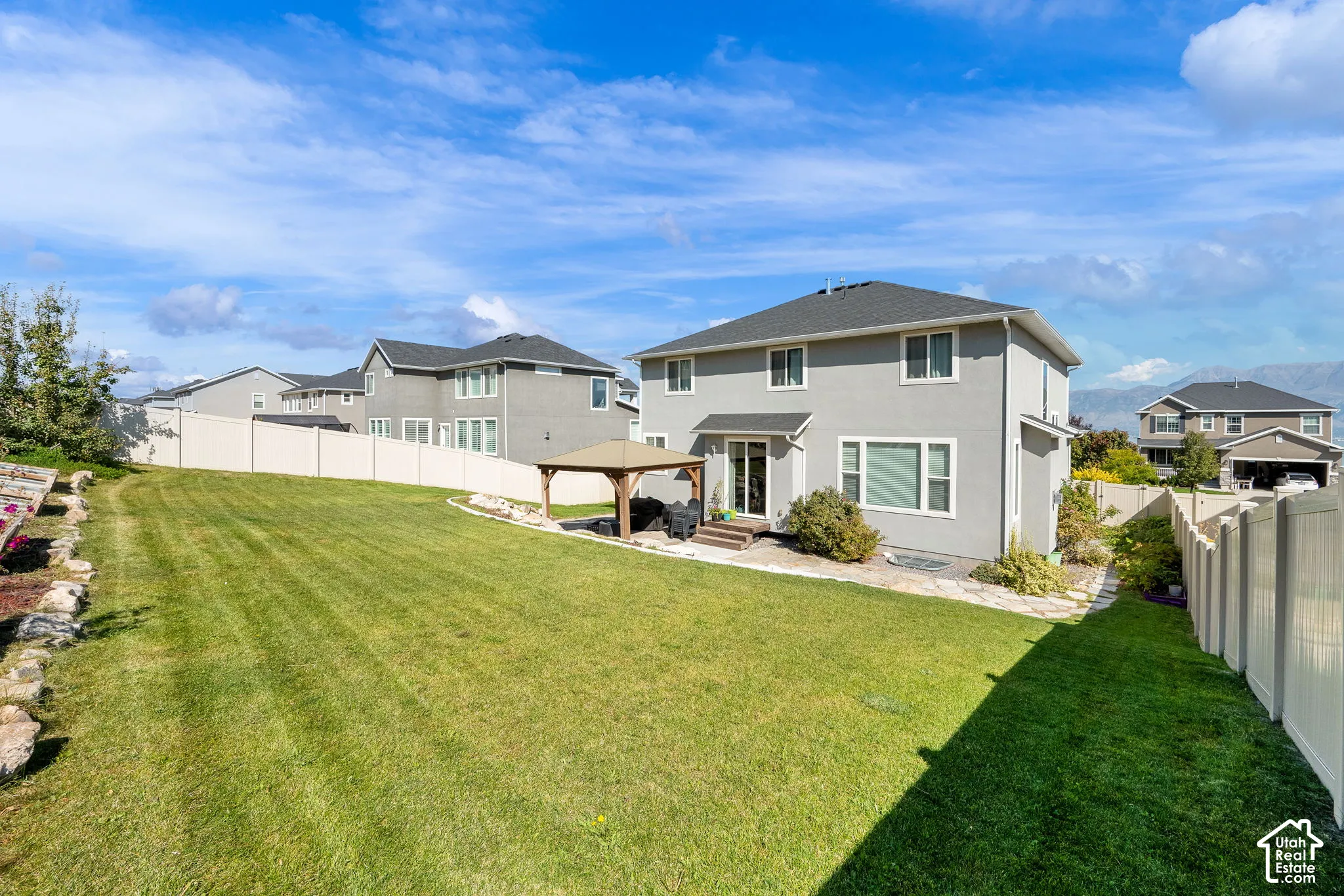 Expansive backyard featuring a sprawling lawn, stone-paver patio, permanent wooden gazebo, and surrounding privacy fencing