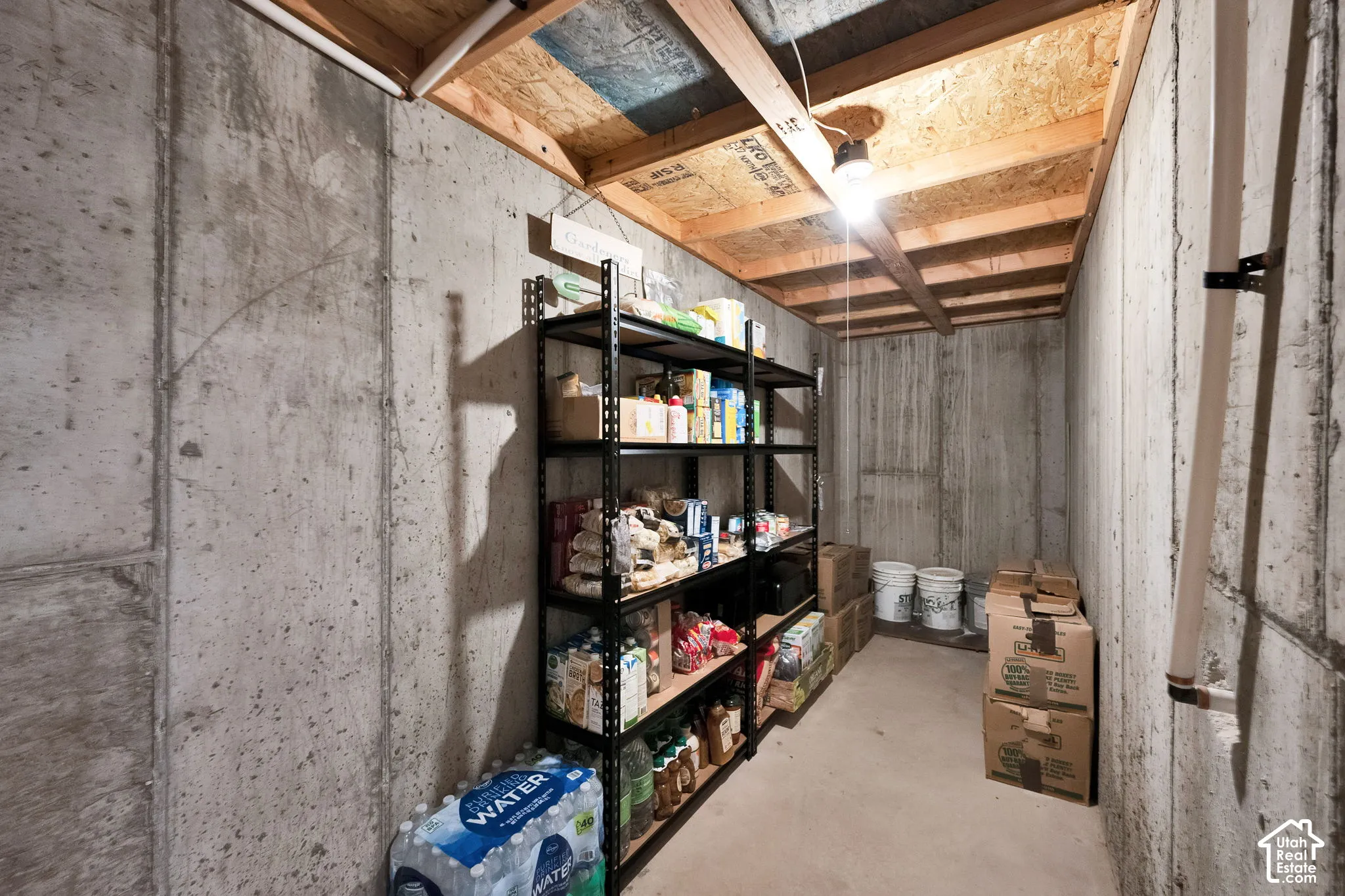 Storage room featuring poured concrete walls and exposed wood-joist ceiling