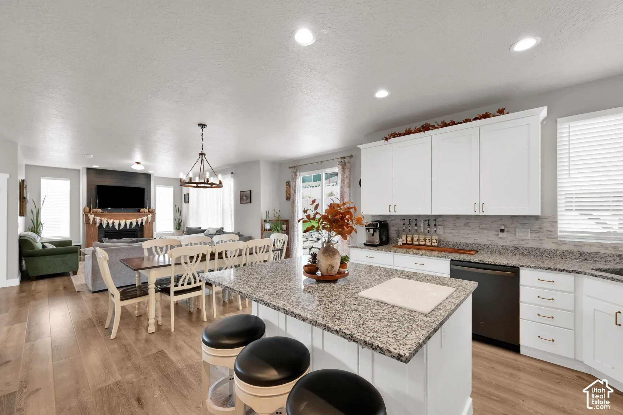 Open-concept kitchen featuring white shaker-style cabinetry, stone-surface countertops, a center island with bar seating, and wood-finish flooring, complemented by a stone-faced fireplace