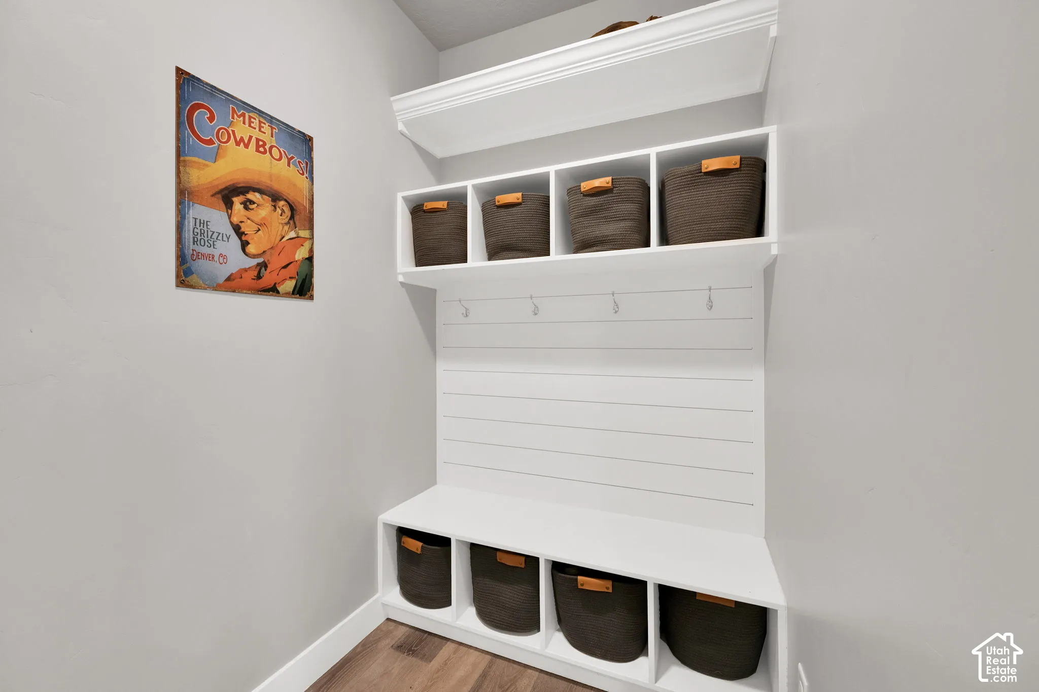 Built-in white cubby unit featuring shiplap detailing, crown molding, integrated coat hooks, and open upper and lower storage shelving