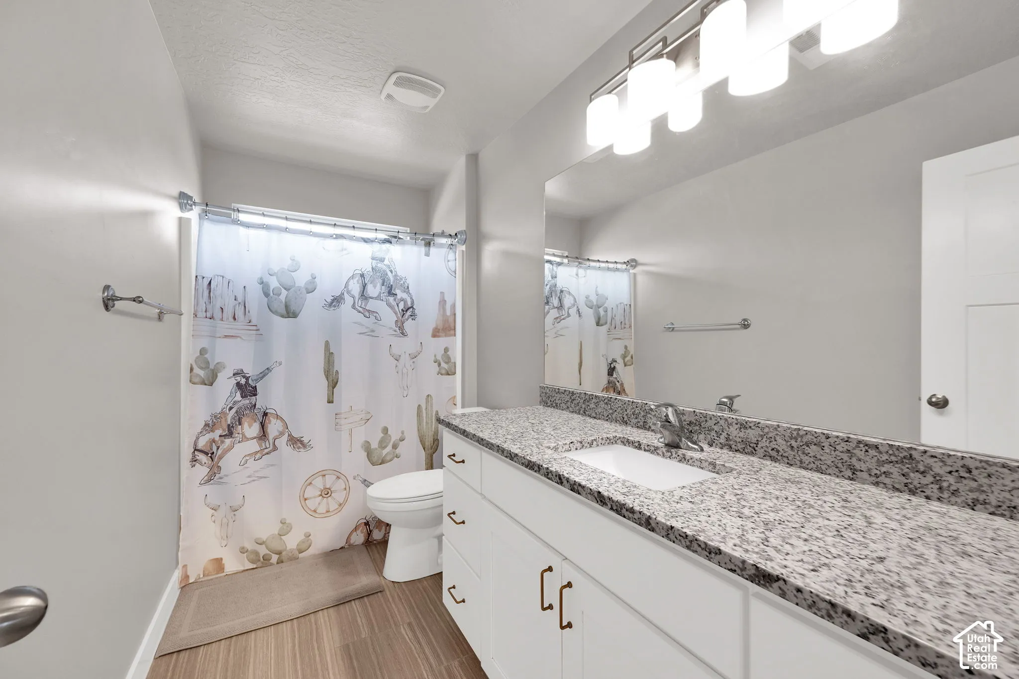 White vanity cabinet featuring a stone-look countertop, integrated rectangular undermount sink, multi-bulb light fixture, and wood-finish flooring
