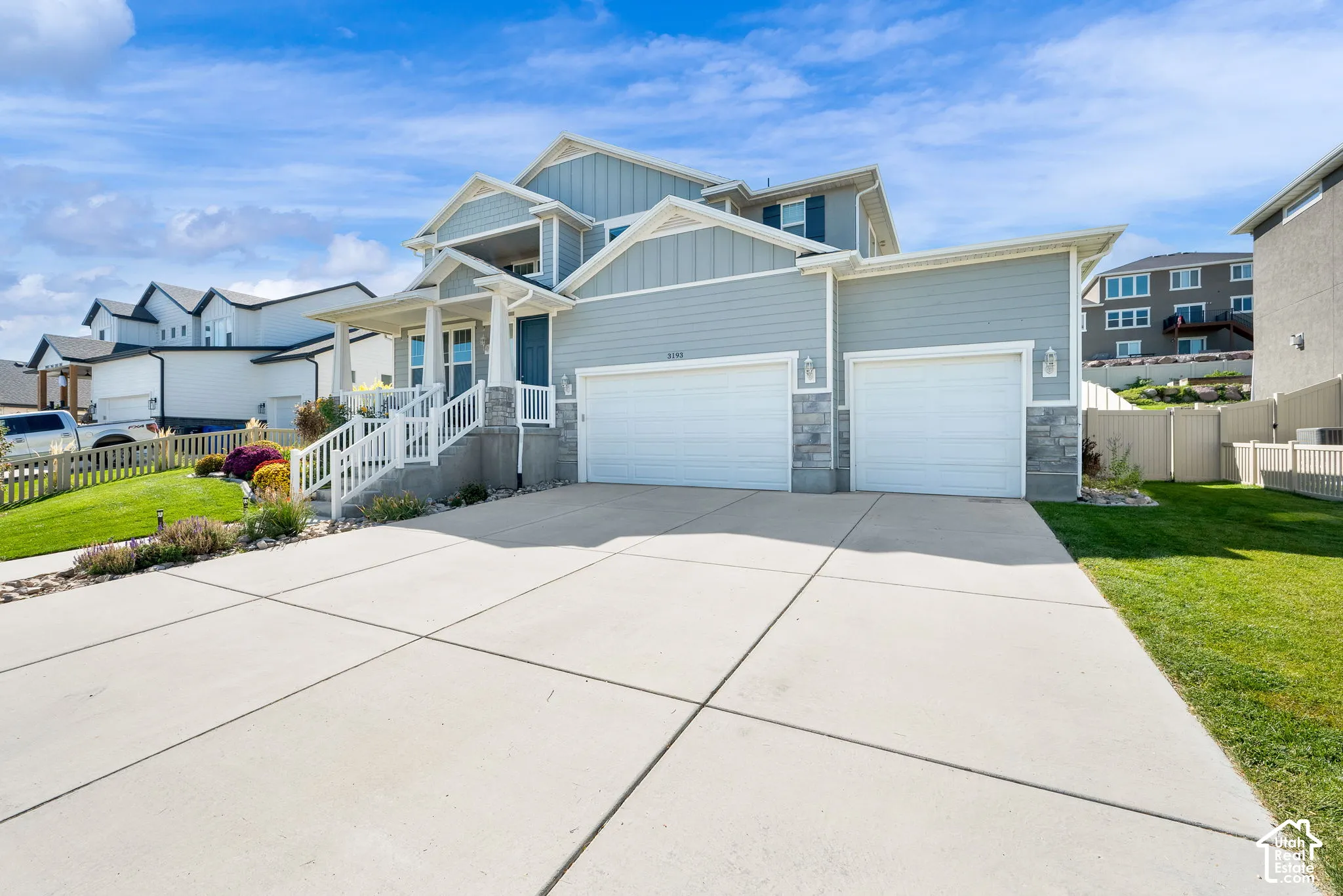 Multi-level exterior featuring horizontal and vertical siding, stone veneer accents, a covered front porch with white railing, and a three-car attached garage