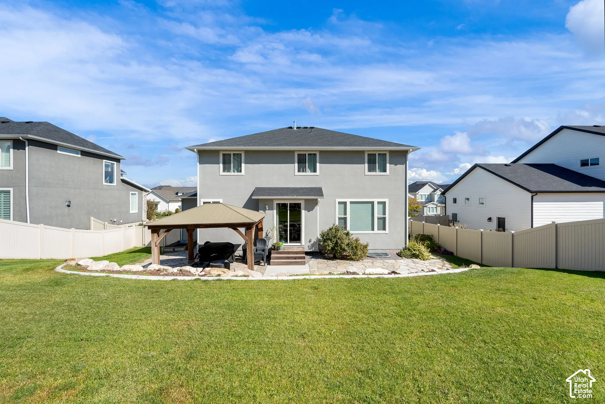 Rear exterior featuring a covered gazebo, stone patio, stone landscape border, and full-height perimeter fencing