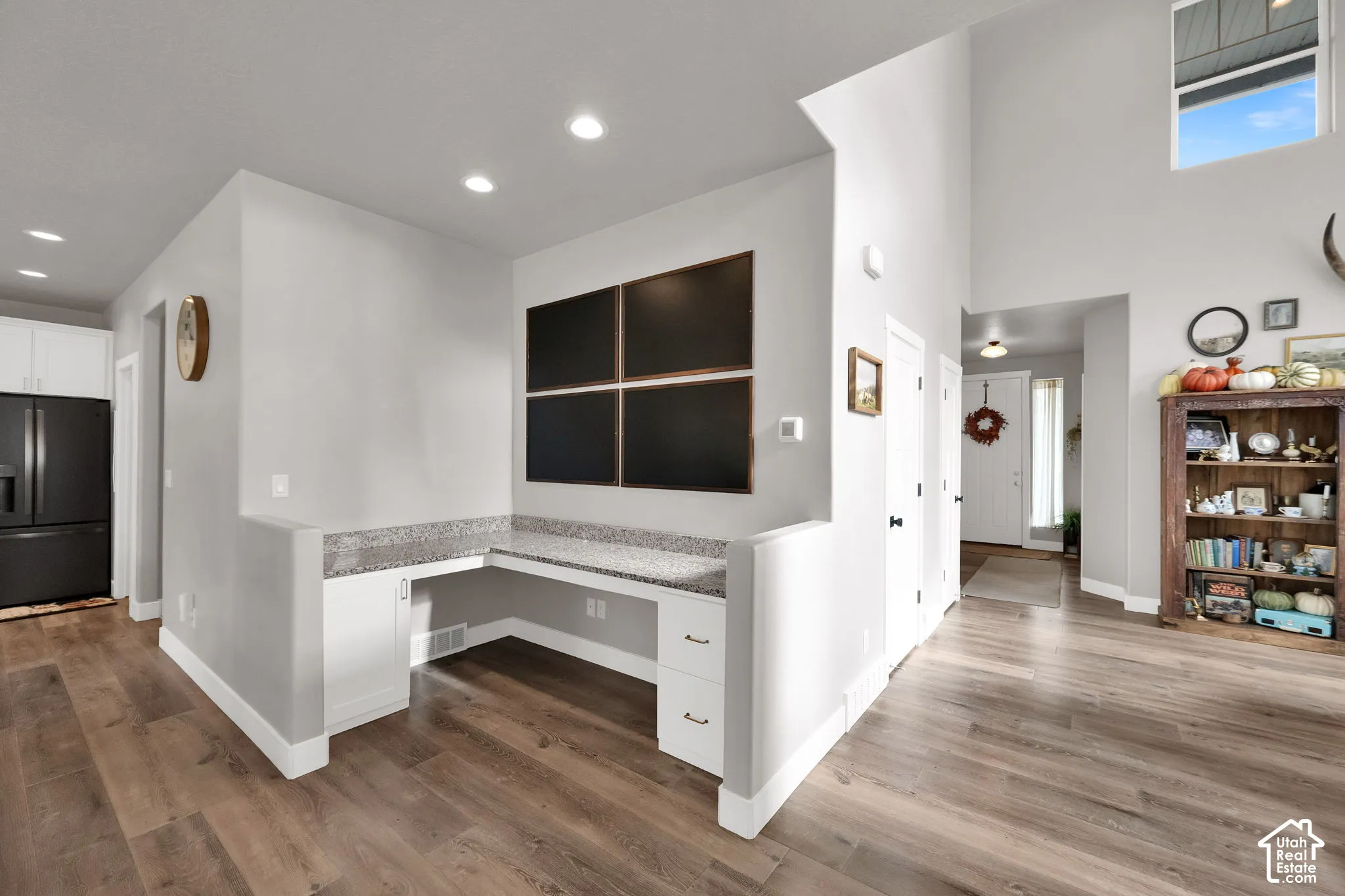 Built-in L-shaped desk with stone countertop, white cabinetry, recessed lighting, and wood-finish flooring under vaulted ceilings