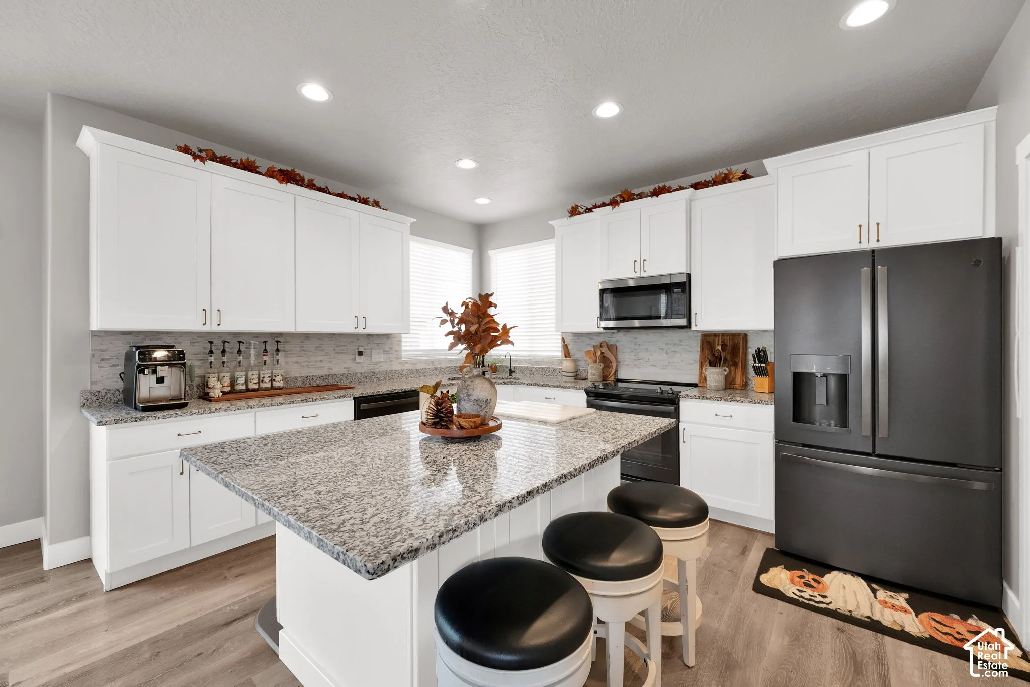 Kitchen featuring white cabinetry, stone countertops, a center island with bar seating, matte black appliances, and recessed lighting