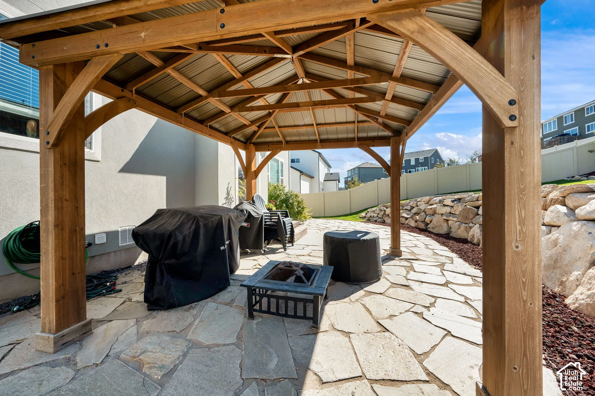 Outdoor living space featuring a timber-frame gazebo with a corrugated metal roof, stone paver patio, and natural rock retaining wall