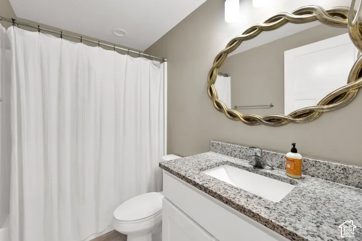 Bathroom featuring a white vanity cabinet with stone-composite countertop, integrated rectangular sink, wall-mounted oval mirror with gold-tone twisted frame, and chrome fixtures