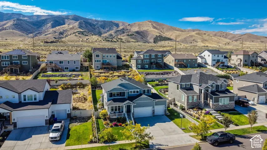 Aerial perspective featuring a multi-story residence with a multi-car garage, pitched shingle roof, stone and siding facade, and landscaped front lawn set against a mountainous backdrop