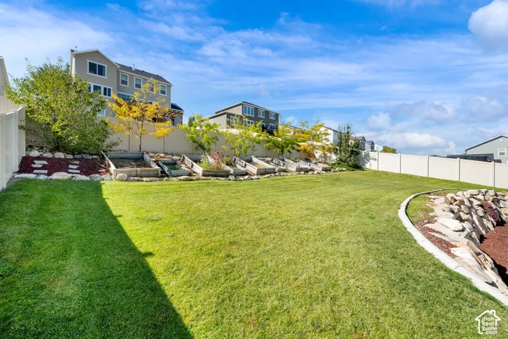 Backyard featuring a manicured lawn, tiered garden beds, stone hardscaping, and perimeter privacy fencing