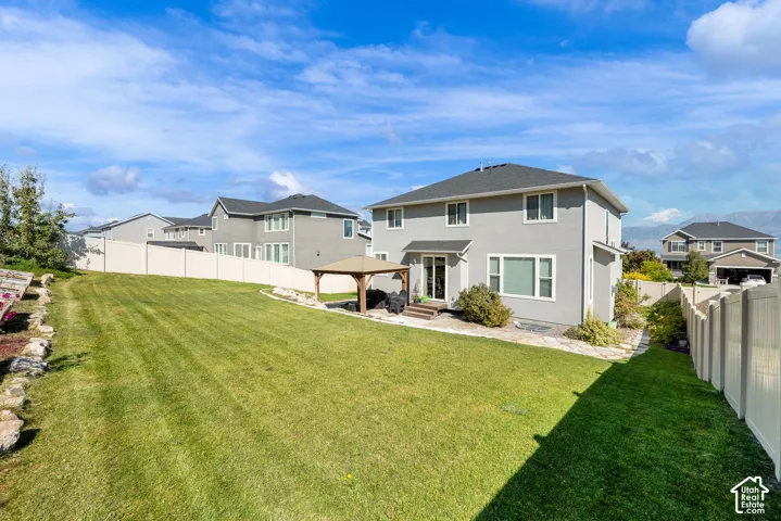Expansive backyard featuring a sprawling lawn, stone-paver patio, permanent wooden gazebo, and surrounding privacy fencing