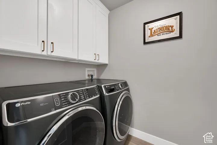 Laundry room featuring white shaker-style wall cabinetry with metallic pulls and wood-finish flooring