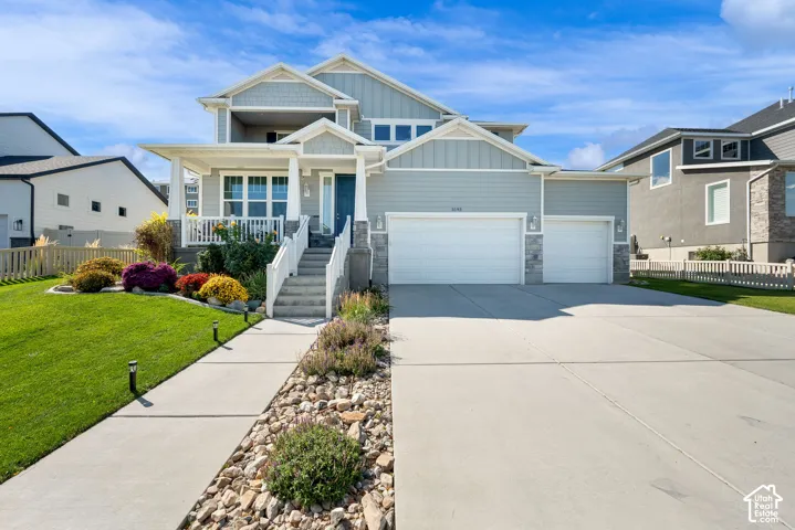 Two-story exterior featuring horizontal siding, stone veneer accents, a covered front porch with white railing, and an attached three-car garage
