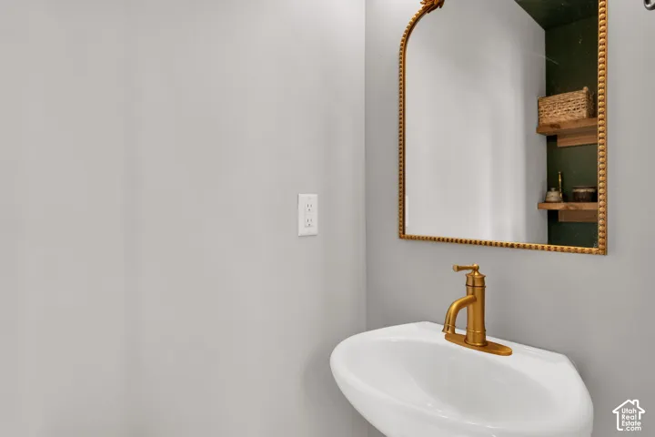 Wall-mounted sink featuring a brass-finish single-handle faucet, arched mirror with a beaded gold-tone frame, and built-in recessed shelving