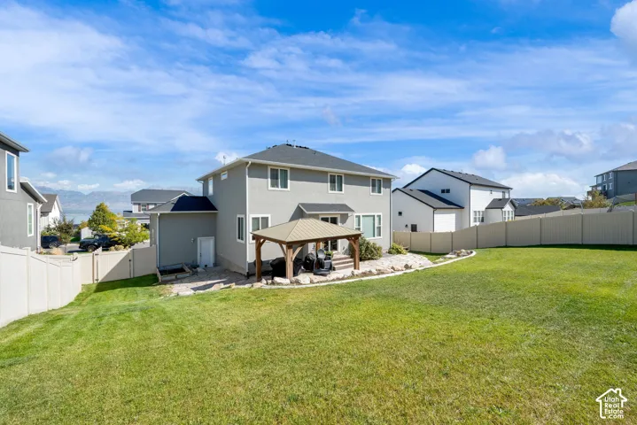 Expansive backyard featuring a manicured lawn, stone-accented patio, permanent gazebo structure, and perimeter vinyl fencing