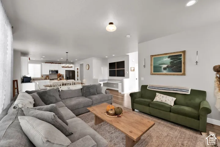 Open-concept interior featuring recessed lighting, wood-finish flooring, white kitchen cabinetry, a dedicated built-in desk area, and a decorative chandelier