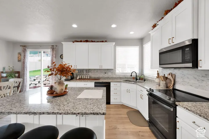 Kitchen featuring white shaker cabinetry, stone-patterned countertops, a center island with seating space, recessed lighting, and wood-finish flooring