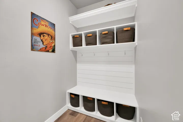 Built-in white cubby unit featuring shiplap detailing, crown molding, integrated coat hooks, and open upper and lower storage shelving
