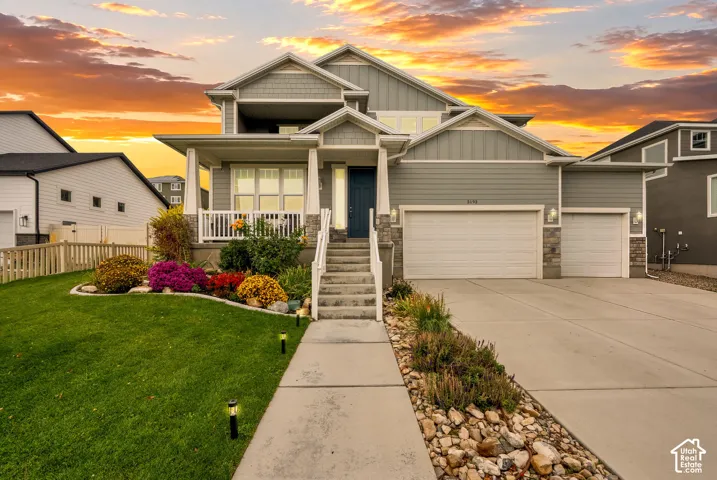 Multi-level exterior featuring horizontal lap and shingle siding, stone veneer accents, a covered front porch with white railing, and a three-car garage