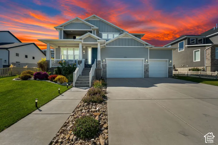 Two-story residence featuring horizontal lap siding, stone veneer accents, a covered front porch with white railing, and a three-car garage