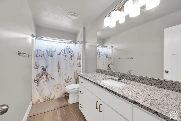 White vanity cabinet featuring a stone-look countertop, integrated rectangular undermount sink, multi-bulb light fixture, and wood-finish flooring