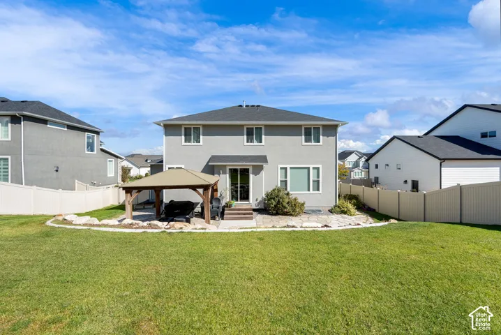 Rear exterior featuring a covered gazebo, stone patio, stone landscape border, and full-height perimeter fencing