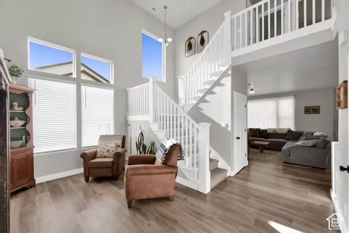 Double-height ceiling, wood-finish flooring, white staircase with balustrade, expansive multi-pane windows, and open upper-level mezzanine