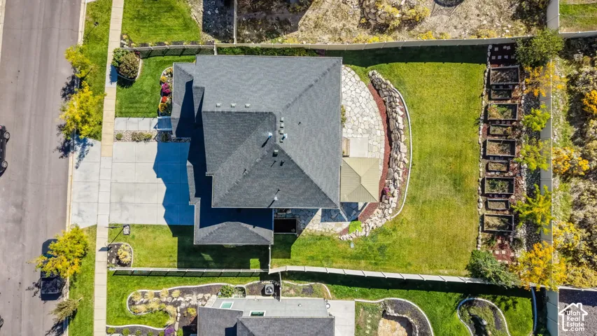 Aerial perspective featuring a manicured lawn, stone-paved patio, stacked stone retaining wall, and raised garden beds enclosed by perimeter fencing