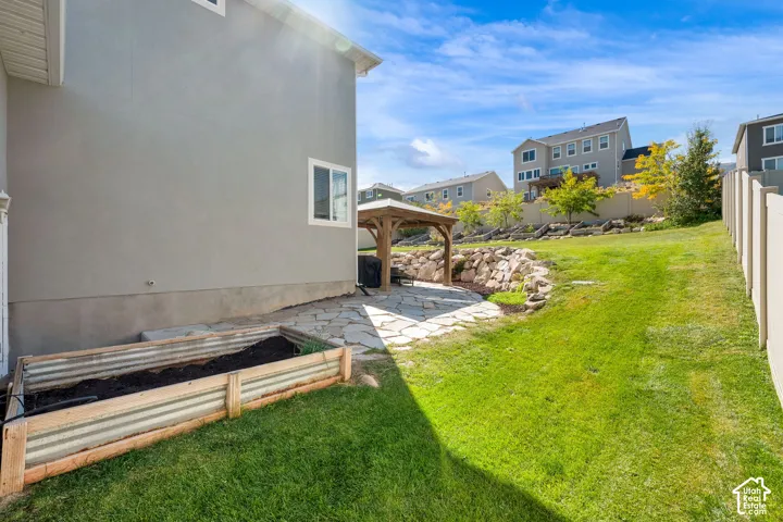 Rear yard featuring a stone patio, detached wooden pergola, tiered rock landscaping, and a corrugated metal raised garden bed