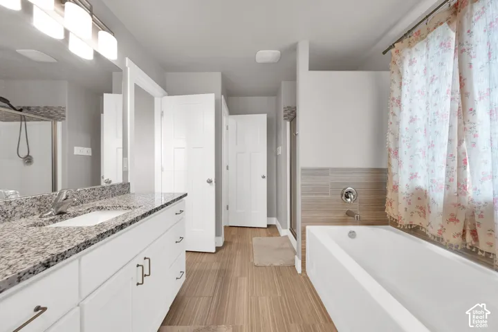 Bathroom featuring white cabinetry, stone-surface countertop, wood-finish flooring, undermount sink, and tiled bathtub surround