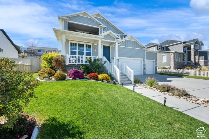 Two-story residence featuring lap siding, cedar-shake accents, a covered front porch with white railing, and a three-car garage
