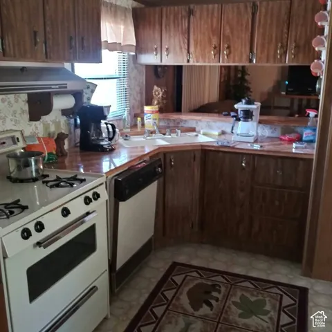 Kitchen featuring wood-grain cabinetry, laminate countertops, a double-basin sink, a freestanding gas range, and a built-in dishwasher