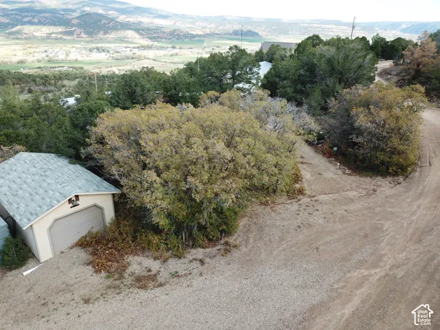 Detached garage with shingled roof, gravel driveway, and mature trees, set against a mountainous landscape