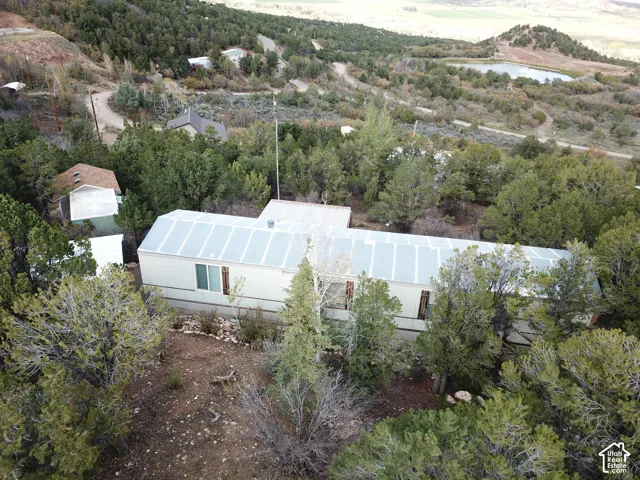 Single-story residence featuring a metal roof, light-colored siding, and a hillside setting surrounded by mature evergreen trees