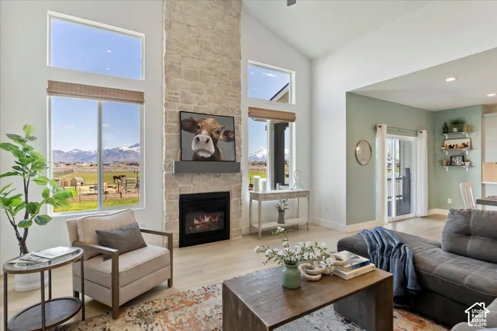Vaulted ceilings, full-height natural stone fireplace, floor-to-ceiling windows, light wood-finish flooring, and mountain backdrop