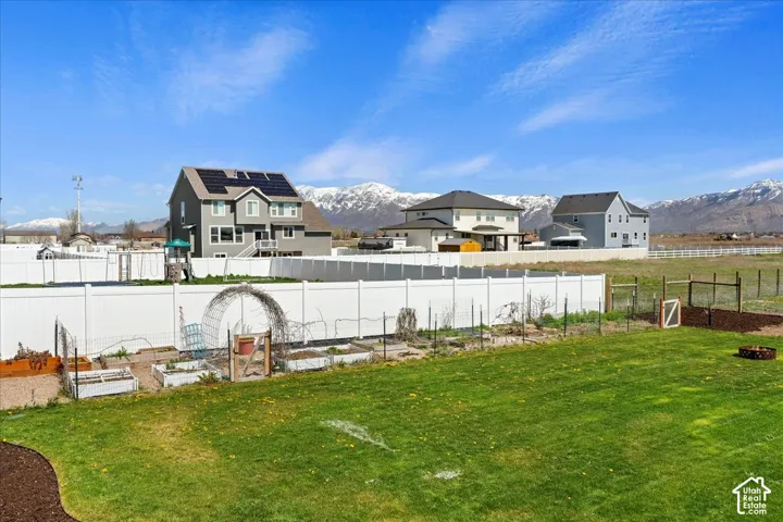 Expansive fenced backyard featuring a grass lawn, built-in garden beds, metal garden trellis, and mountain backdrop