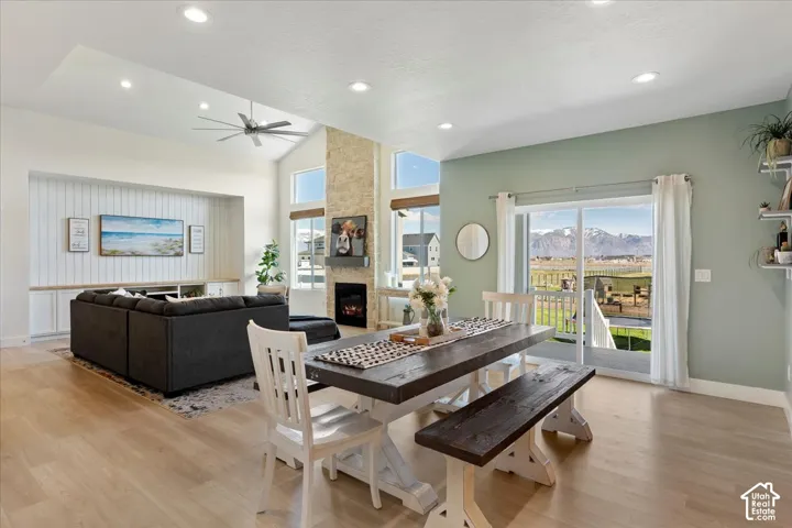 Open-concept living space featuring vaulted ceilings with recessed lighting, a stone-surround fireplace, wood-finish flooring, built-in cabinetry with vertical paneling, and sliding glass doors revealing a mountain backdrop