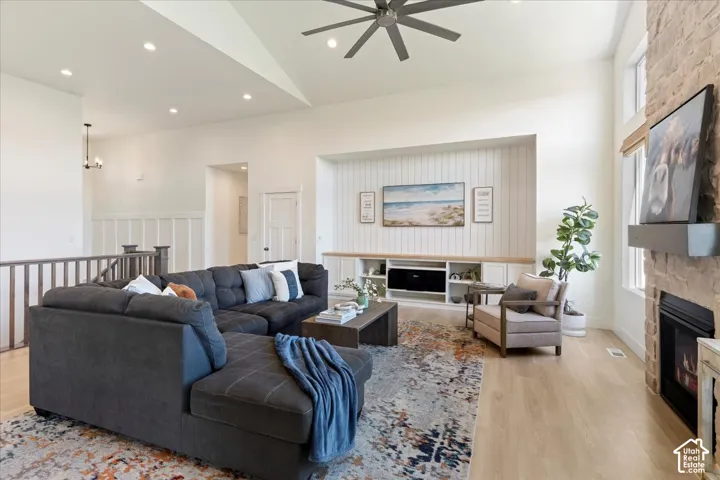Vaulted ceiling with an integrated multi-blade fan, stone-surround fireplace, floor-to-ceiling hearth, built-in media cabinetry with vertical plank detailing, and light-toned wood-finish flooring