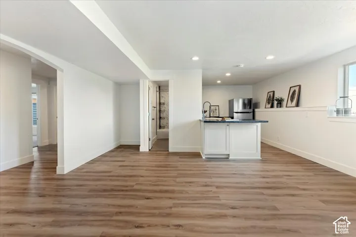 Open floor plan featuring wood-finish flooring, recessed lighting, and a kitchen area with white cabinetry, a countertop, and a stainless steel refrigerator